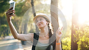 Funny tourist girl in hat taking selfie photos with smartphone camera during travelling and hitchhiking