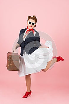 Funny traveler girl with suitcase and black sunglasses. Brunette woman in pin-up style with vintage case.