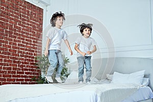 Funny twins. Energetic little latin boys, brothers having fun together, jumping on the bed at home