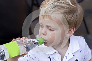 Funny two year baby boy is drinking water from a bottle.