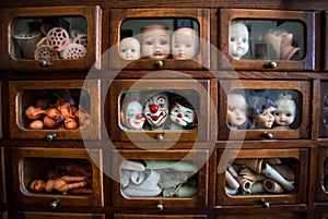 Funny and ugly faces of dolls inside wooden house with small windows. Many parts of heads and legs inside small boxes