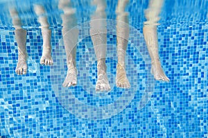 Funny underwater family legs in swimming pool, under water view of mother and kids, vacation fitness