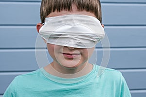 A funny view of a boy wearing white protective surgical medical mask on his eyes instead of a mouth, he prank epidemia photo