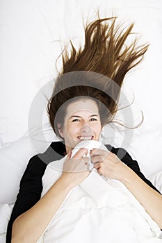 Funny wakening. Young woman is lying in her bed, smiling and joking.