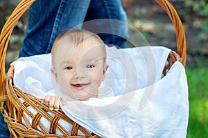 Funny walk outdoor: Portrait of a happy smiling baby sitting in a big wicker basket outdoor. Father is carrying the basket