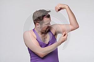 Funny weak sportsman exercising looking on his biceps