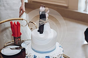 Funny wedding cake topper, figurines of bride and groom tied together with a rope, fun wedding moment with delicious white cake