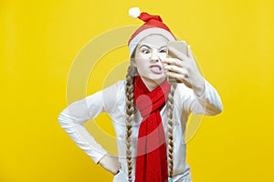 Funny Winsome Caucasian Teenage Girl With Cellphone Taking Selfie While Making Gimmick And Wearing Christmas Santa Hat And Posing