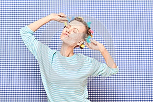 Funny woman with colorful hair curlers, and skincare product on face