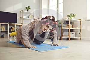 Funny woman in curlers doing push-ups on fitness mat during sports workout at home