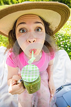 Funny woman drinking green detox smoothie on picnic. Face close up portrait outdoor.