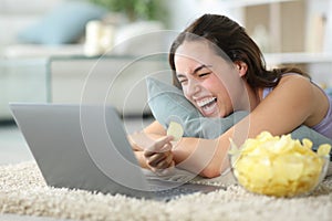 Funny woman eating chips watching media on laptop photo