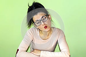A funny woman with glasses makes stupid faces on a green background.