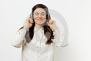 funny woman in light shirt stands listening to music in her headphones, closing her eyes with pleasure and holding