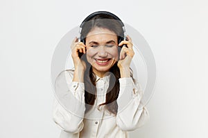 funny woman in light shirt stands listening to music in her headphones, closing her eyes with pleasure and holding