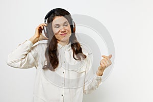 funny woman in light shirt stands listening to music in her headphones, closing her eyes with pleasure and holding