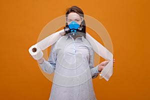 funny woman with with toilet paper in hand in protective equipment in medical mask on yellow background, coronavirus pandemic,