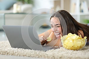 Funny woman watching media on laptop eating chips photo