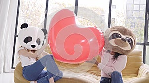 Funny women wearing animal mask bear panda holding big heart at home - Happy positive emotions people together