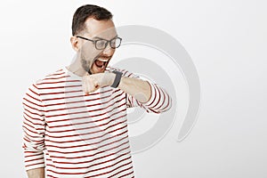 Funny yelling european man in glasses, raising arm near face and shouting at black digital watch, making command to