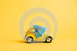Funny yellow retro car with beach umbrella on yellow background. Summer vacation concept.