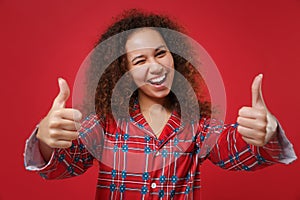 Funny young african american girl in pajamas homewear posing while resting at home isolated on red wall background