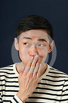 Funny young Asian man covering his mouth by palm