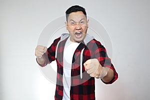 Funny young Asian man showing cynical unhappy angry facial expression putting up his fist challenge to fight