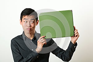 Funny young Asian man showing green copy space box and looking s