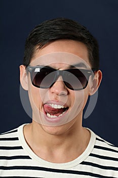 Funny young Asian man in sunglasses showing his tongue