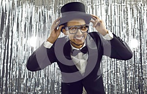 Funny young black man in a dinner suit, top hat and glasses having fun at a party