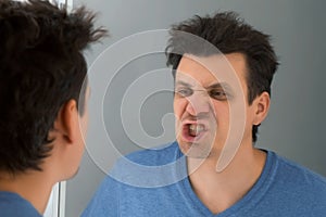 Funny young brunet handsome man is looking on his teeth at mirror reflection.