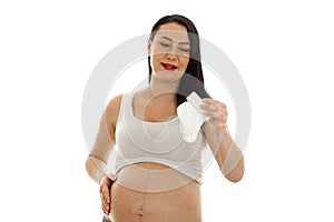 Funny young brunette pregnant girl with little white socks in her hands posing isolated on white background