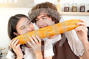 Funny young couple eating bread together in kitchen Young man and beatuiful woman are laughing each other during eating bread