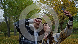 Funny young couple in love taking selfie on their mobile phone in autumn park.