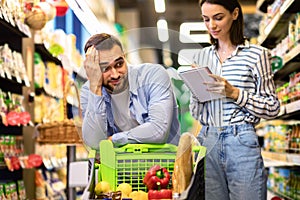 Funny young couple with shopping list in supermarket