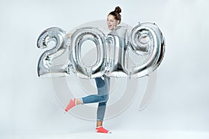 Funny young girl dressed in white t-shirt, jeans and pink socks holding balloons in the shape of numbers 2019 on the