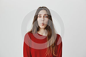 Funny young girl with popped eyes imitating fish, folding her lips and popping eyes, isolated over white background