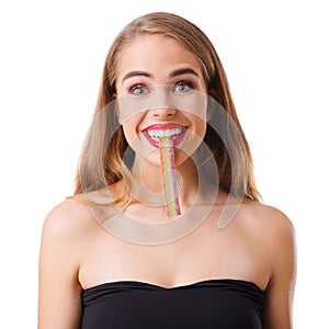 A funny young girl is holding in her teeth an acid marmalade sugar ribbon. Isolated on white background.