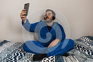 Funny young guy in a fantastic pyjama in his bedroom. He is taking a selfie