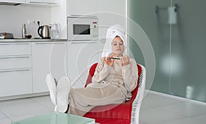 Funny young housewife with bathtowel on her head sitting in the chair doing manicure