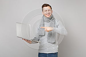 Funny young man in gray sweater, scarf with closed eyes work pointing index finger on laptop pc computer on