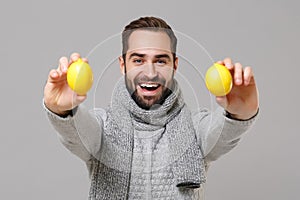 Funny young man in gray sweater, scarf posing isolated on grey wall background, studio portrait. Healthy fashion