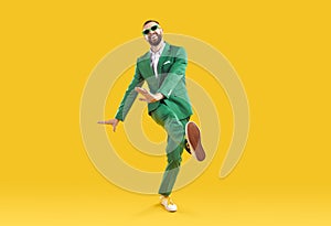 Funny young man in a green party suit and sunglasses dancing on a yellow background