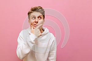 Funny young man isolated on pink background, looks away at copy space with pensive face. Pensive guy stands on a pink background