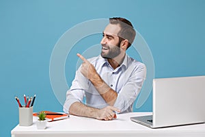 Funny young man in light shirt sit, work at desk with pc laptop isolated on pastel blue background. Achievement business