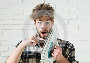 Funny young man in plaid shirt touches iron with his finger and screams. Husband burning clothing while ironing.