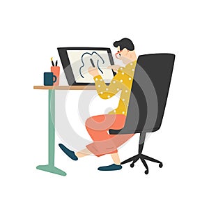 Funny young man sitting at desk and drawing on graphic tablet. Digital designer, illustrator or freelancer working at