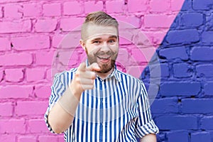 Funny young stylish guy with a mustache and a beard in a stylish shirt posing on of a blue-purple brick wall and