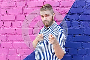 Funny young stylish guy with a mustache and a beard in a stylish shirt posing on of a blue-purple brick wall and